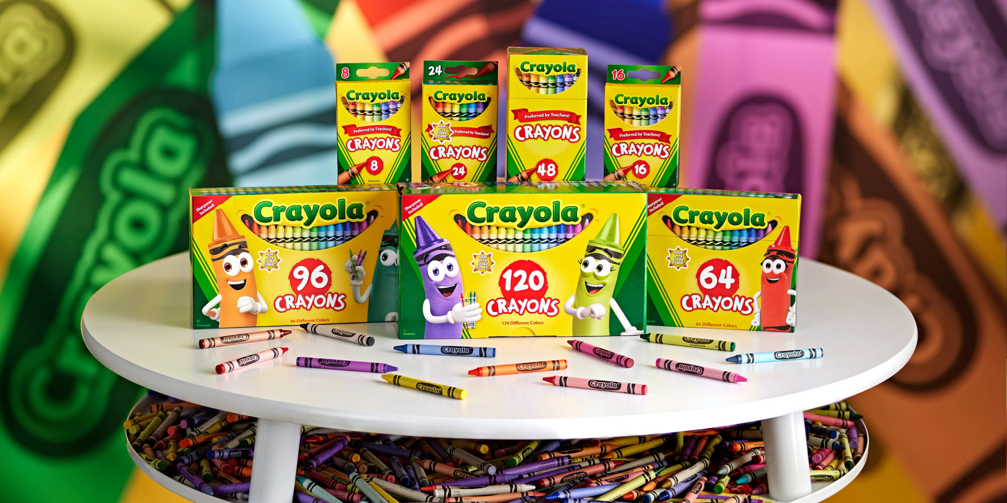 Photo of multiple packs of Crayola crayons sitting on a table with multiple single crayons in front of them